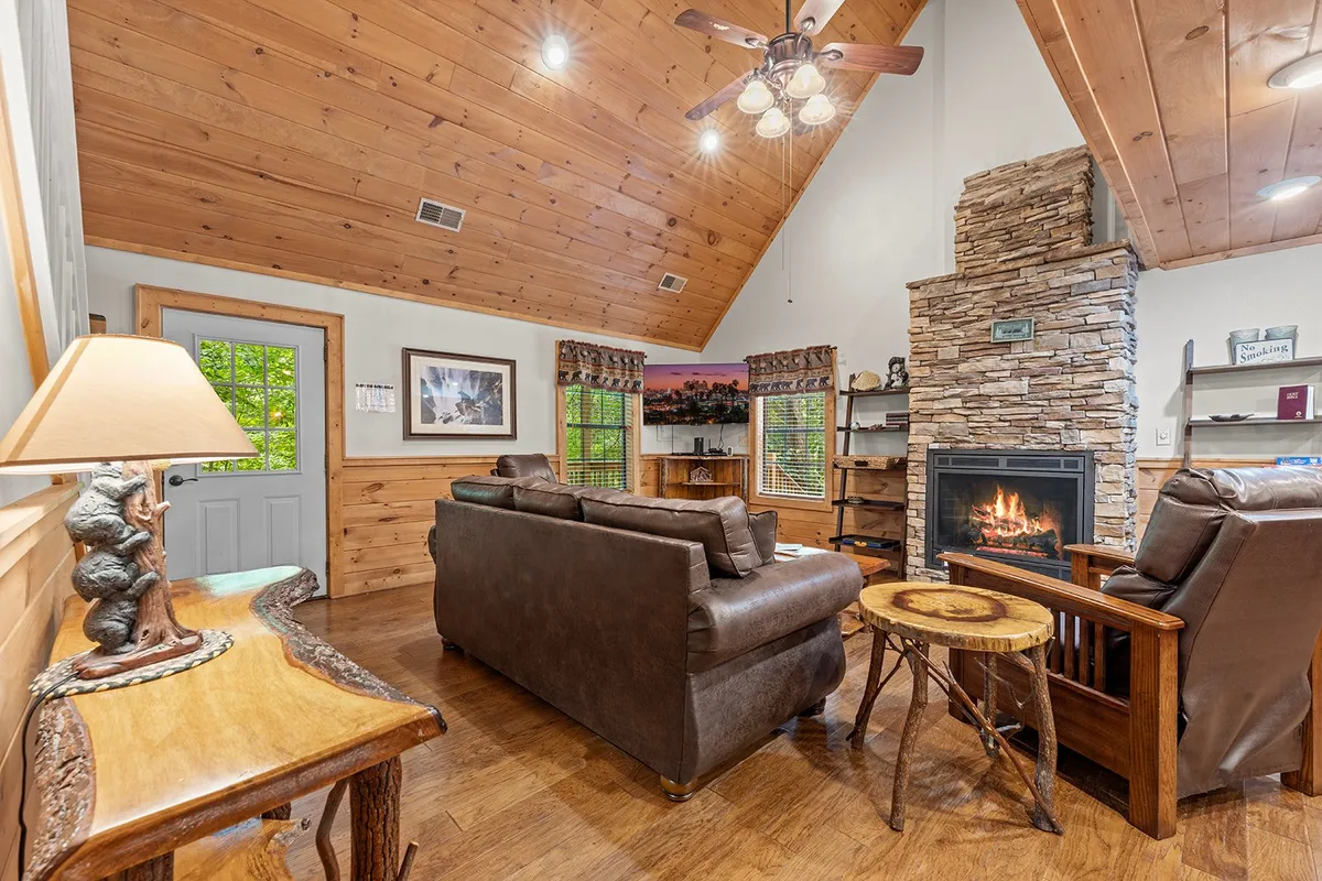 A cozy interior living area featuring a prominent stone fireplace, comfy leather sofa, warm wooden ceiling, and a decorative lamp, all exuding rustic charm and inviting warmth.