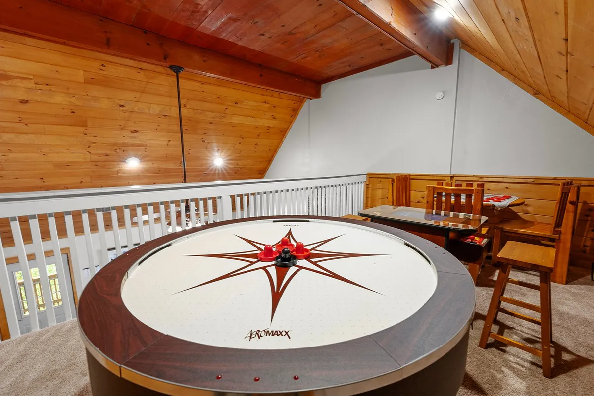 An air hockey table sits prominently in a warmly decorated loft space, with bar stools and a dining table in the background. The area looks ready for spirited matches and relaxed group gatherings.