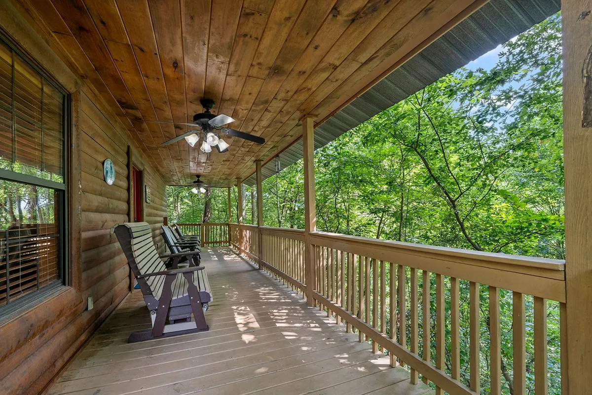 A wide wooden deck with two inviting rocking chairs, a ceiling fan overhead, and views of dense surrounding trees. The space is ideal for sipping coffee, reading a book, or simply appreciating the sights and sounds of the forest.
