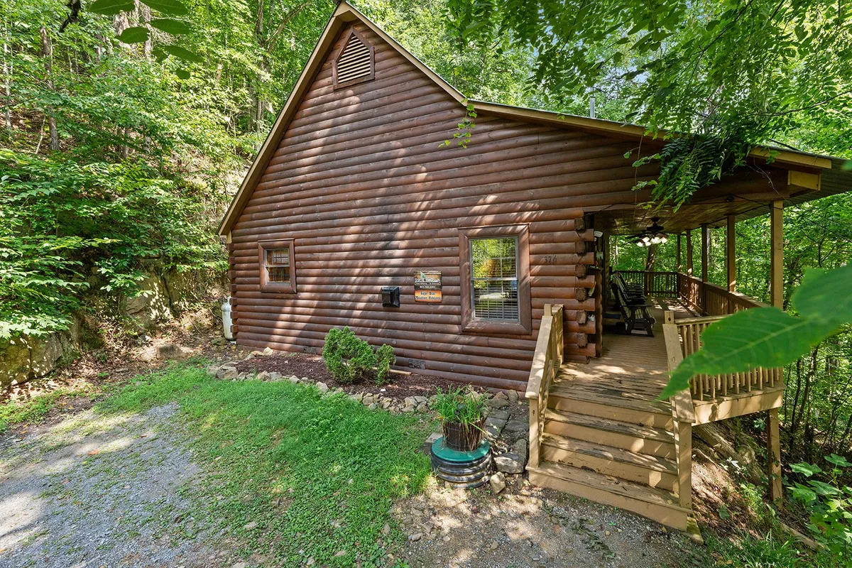 A charming log cabin with a wooden porch set amidst lush greenery. The inviting porch and rustic exterior highlight the cabin’s connection to nature and the great outdoors, making it an ideal base for family adventures in Pigeon Forge.
