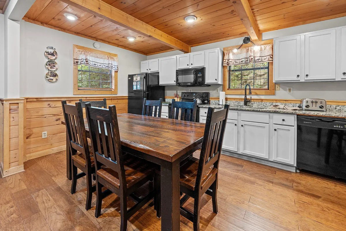 A spacious, cozy dining area with a wooden dining table, black appliances, granite countertops, and wood cabinetry. The setting is perfect for shared meals, game nights, or planning your day's excursions, highlighting the practical amenities for budget-conscious travelers.