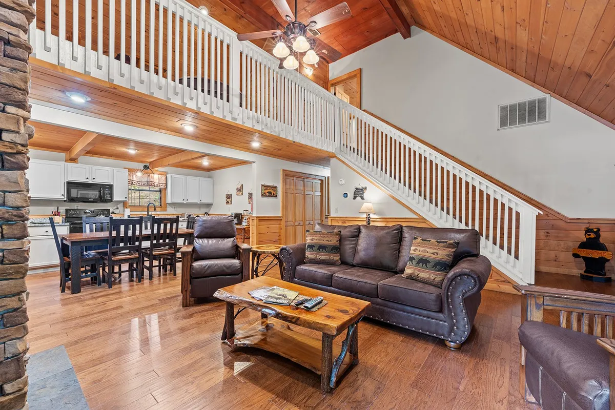 A view of the living room featuring a comfortable sofa, coffee table, and a glimpse of the dining area and staircase. The setting feels inviting and is ideal for both relaxation and socializing, with plenty of natural light enhancing the welcoming ambiance.