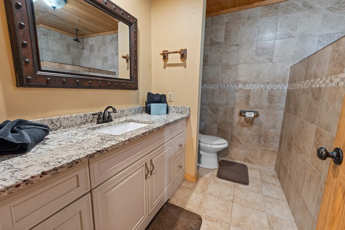A serene bathroom space featuring a granite countertop, large mirror, modern shower area, and toilet. The clean, calming design invites guests to refresh and unwind after an active day.